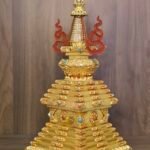 Front view of the Tibetan style stupa with symmetrical curved side ornaments, ribbed spire, and ornate tiered base for altar display.