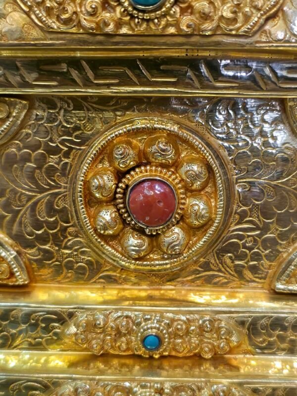 Macro detail of a circular floral medallion with a red center inlay set into an engraved gold plated panel on the stupa base.