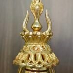 Close up of the finial and crown at the top of the stupa, showing carved detailing and polished gold plated metal surfaces.