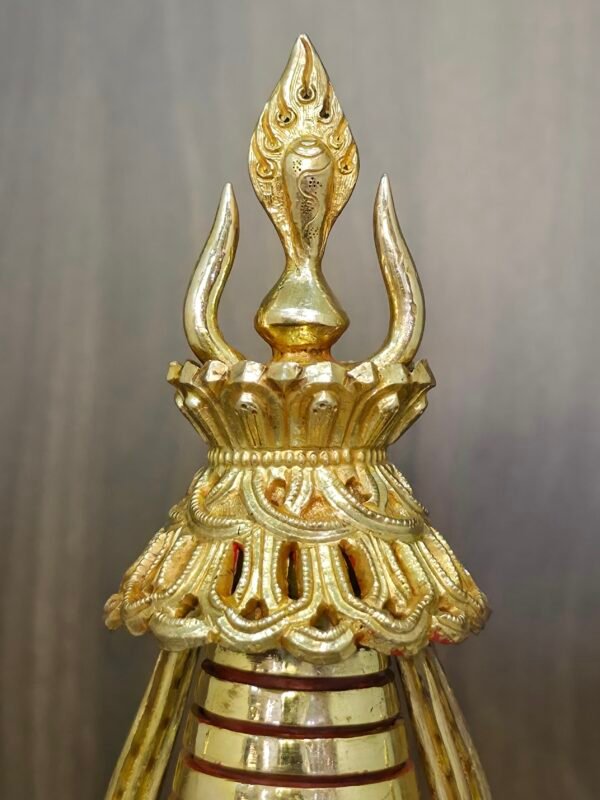 Close up of the finial and crown at the top of the stupa, showing carved detailing and polished gold plated metal surfaces.