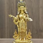 Full front view of Yeshe Tsogyal gold statue holding a kapala offering bowl and standing on a lotus base.