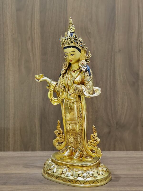 Right side profile of gold plated Yeshe Tsogyal statue holding a kapala offering bowl.