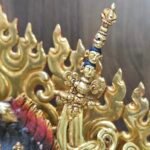 Detail of the trident topped khatvanga staff decorated with three skulls resting on her shoulder.