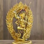 Left view of Dorje Phagmo Vajravarahi statue with gold plated finish, ornate halo and upright staff shown in profile.