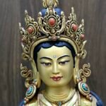 Close facial view of Yeshe Tsogyal statue with coral set crown and raised blessing hand.