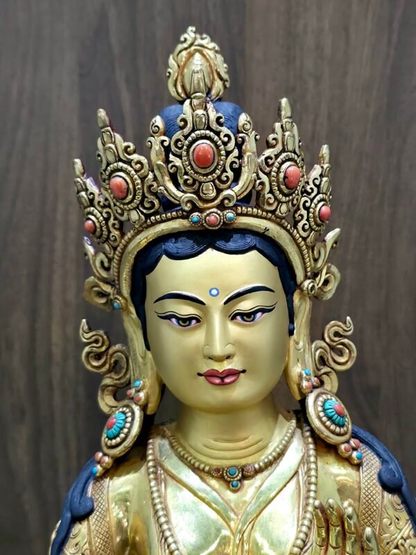 Close facial view of Yeshe Tsogyal statue with coral set crown and raised blessing hand.