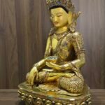 Three quarter front view of Crown Shakyamuni Buddha statue with gold plated copper finish, ornate robe, crown and lotus base.