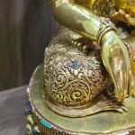 Close up of Crown Shakyamuni Buddha’s robe and right hand, showing detailed engraving and coloured inlay accents.