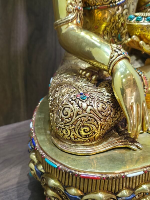 Close up of Crown Shakyamuni Buddha’s robe and right hand, showing detailed engraving and coloured inlay accents.