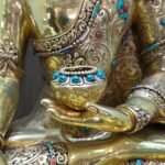 Close up of the alms bowl held by Crown Shakyamuni Buddha, with gold plated hand, engraved robe and coloured inlay.