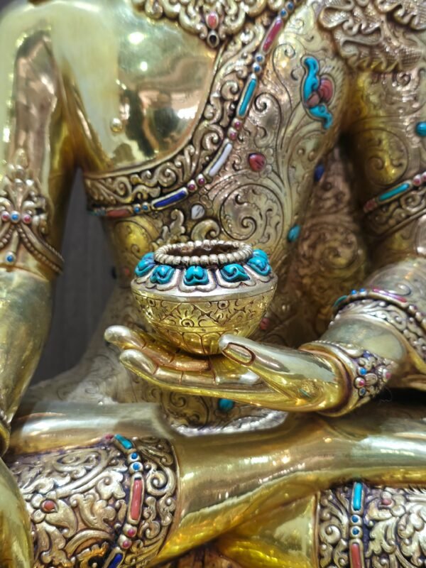 Close up of the alms bowl held by Crown Shakyamuni Buddha, with gold plated hand, engraved robe and coloured inlay.