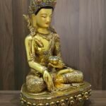 Angled front view of Crown Shakyamuni Buddha statue holding an alms bowl, with gold plated robes and decorative inlay.