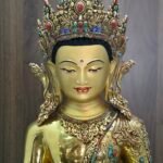 Close up of Crown Shakyamuni Buddha face with gold powder painting, ornate crown, earrings and detailed necklace.