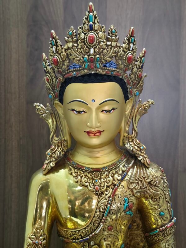 Close up of Crown Shakyamuni Buddha face with gold powder painting, ornate crown, earrings and detailed necklace.