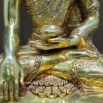 Close-up of the Buddha’s torso and left hand holding the ritual alms bowl, illustrating the intricate patterns on the 24K gold-plated surface.