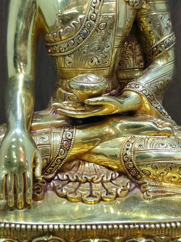 Close-up of the Buddha’s torso and left hand holding the ritual alms bowl, illustrating the intricate patterns on the 24K gold-plated surface.