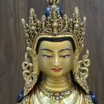 Close-up of Amitayus Buddha’s gold-powder painted face, openwork crown, ornate earrings and red and blue decorative accents.