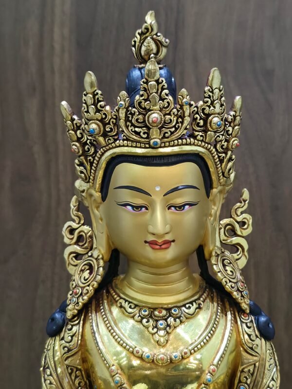 Close-up of Amitayus Buddha’s gold-powder painted face, openwork crown, ornate earrings and red and blue decorative accents.