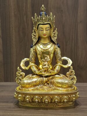 Front view of gold plated Amitayus (Aparimita) Buddha seated on a lotus pedestal, holding a long-life vase beneath an ornate crown.