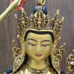 Close-up of Manjushri’s gold-powder-painted face and ornate crown with red and blue decorative accents.