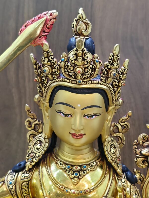 Close-up of Manjushri’s gold-powder-painted face and ornate crown with red and blue decorative accents.