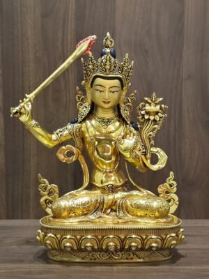 Front view of the gold-plated Manjushri statue seated on a lotus pedestal, with a raised sword and lotus supporting a scripture.