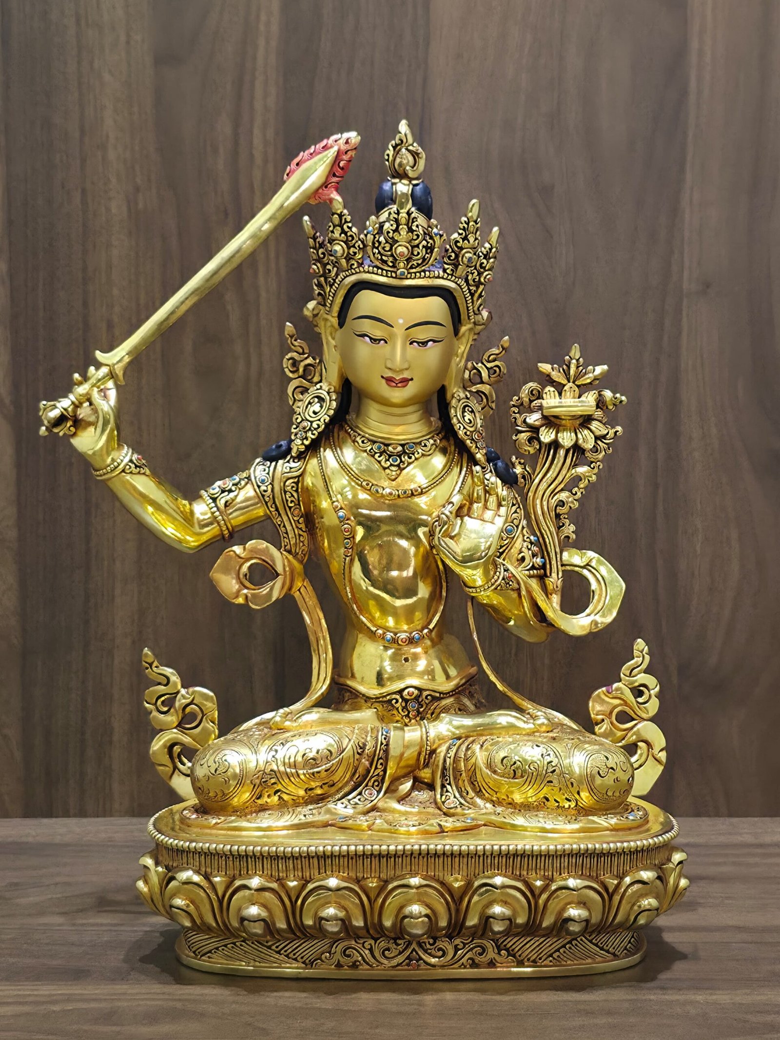 Front view of the gold-plated Manjushri statue seated on a lotus pedestal, with a raised sword and lotus supporting a scripture.