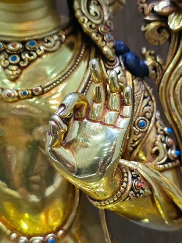Close-up of Manjushri’s raised left hand, with thumb and forefinger touching, beside an ornate bracelet and necklace.