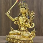 Manjushri statue angled to the left, showing the raised sword, lotus-supported scripture, engraved garments and lotus pedestal.