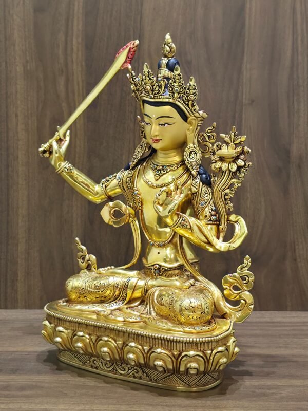 Manjushri statue angled to the left, showing the raised sword, lotus-supported scripture, engraved garments and lotus pedestal.