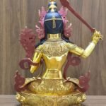 Rear view of the Manjushri statue, showing dark blue hair, red-painted ornament backs and engraved patterns on the garments and base.