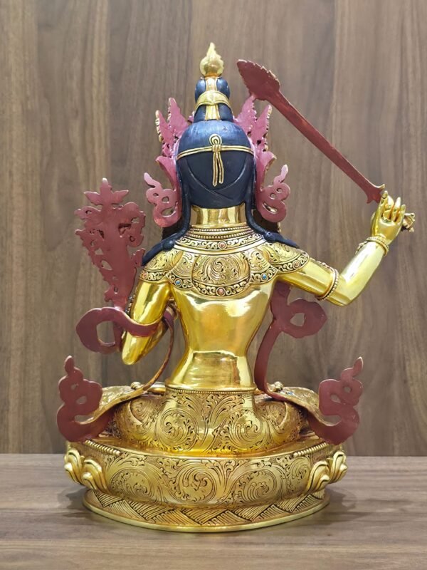 Rear view of the Manjushri statue, showing dark blue hair, red-painted ornament backs and engraved patterns on the garments and base.
