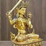 Manjushri statue angled to the right, showing the sword handle, raised hand, flowing scarf and engraved lotus pedestal.