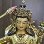 Close-up of Manjushri’s gold-powder-painted face, ornate crown, dark blue hair and earrings with coloured inlays.