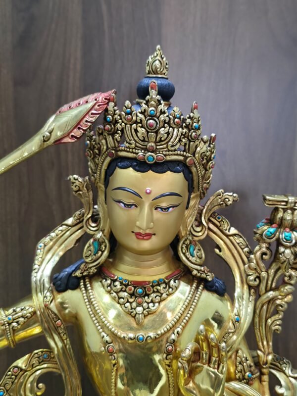 Close-up of Manjushri’s gold-powder-painted face, ornate crown, dark blue hair and earrings with coloured inlays.
