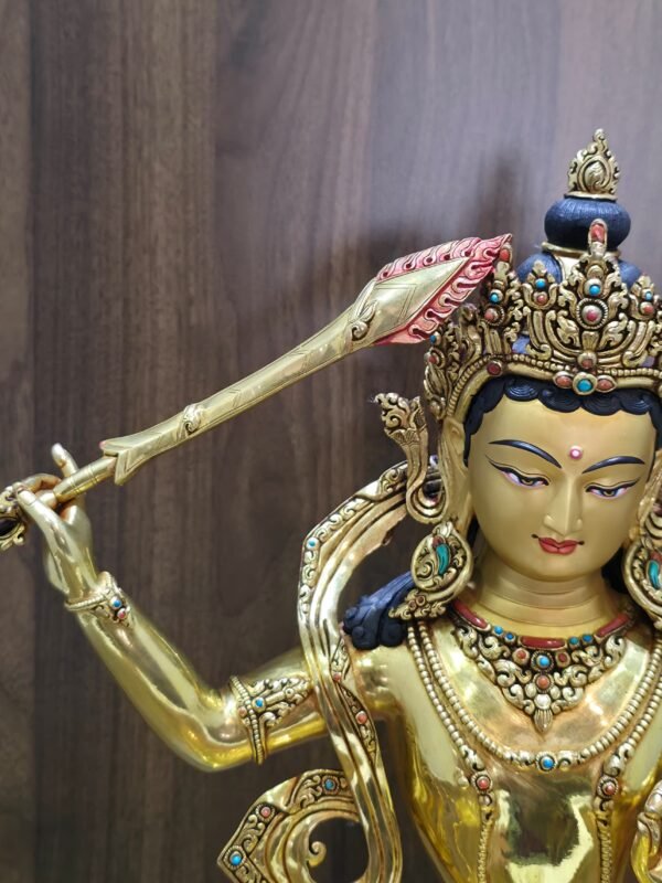 Close-up of Manjushri’s raised sword, showing engraved details along the gold-plated blade and red flames around its tip.