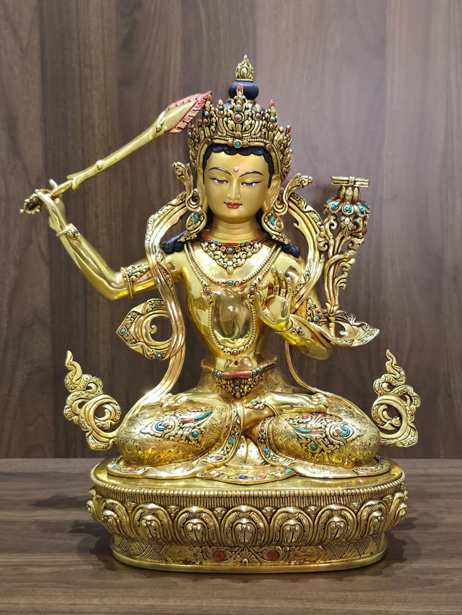 Front view of the gold-plated Manjushri statue seated on a lotus pedestal, with a raised sword and scripture supported by a lotus.