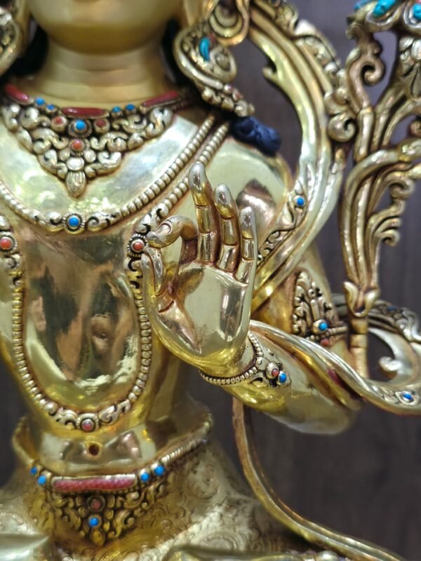 Close-up of Manjushri’s raised left hand, with thumb and forefinger touching, beside layered necklaces and a decorated bracelet.