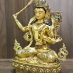 Manjushri statue angled to the left, showing the lotus-supported scripture, curling scarf, coloured garment inlays and lotus pedestal.