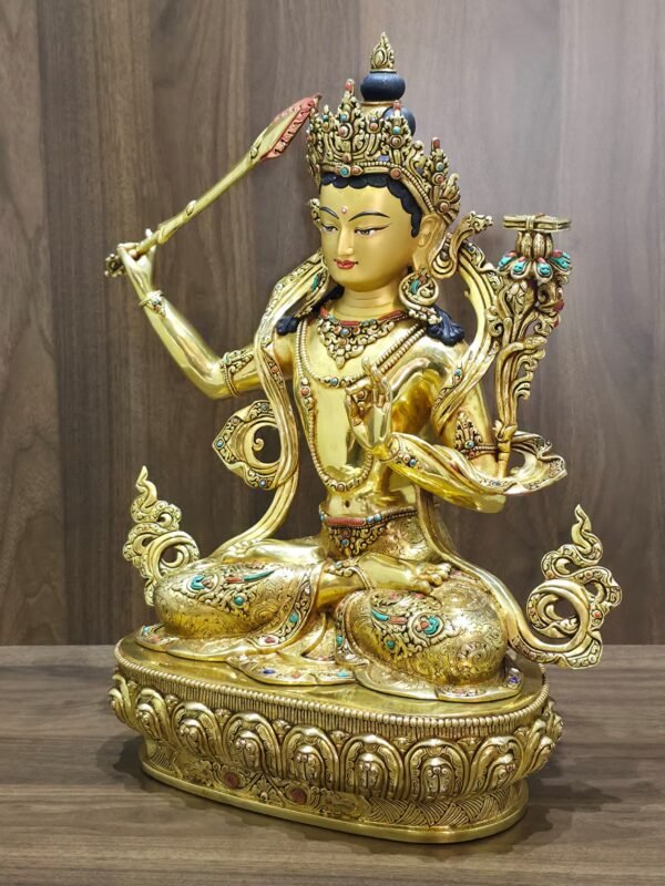 Manjushri statue angled to the left, showing the lotus-supported scripture, curling scarf, coloured garment inlays and lotus pedestal.