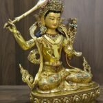 Manjushri statue angled to the right, showing the raised sword, open left palm, layered jewellery and decorated lotus pedestal.