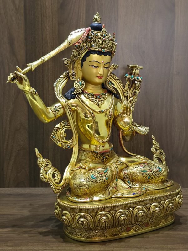 Manjushri statue angled to the right, showing the raised sword, open left palm, layered jewellery and decorated lotus pedestal.