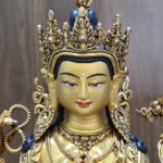 Close-up of Chenrezig statue’s gold-painted face, ornate crown, earrings and red and blue decorative accents.