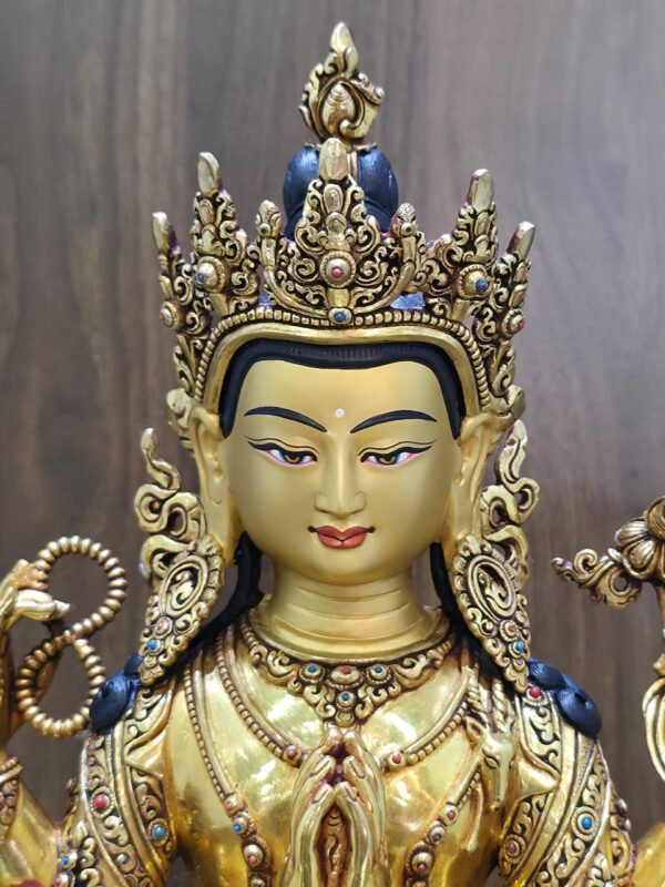 Close-up of Chenrezig statue’s gold-painted face, ornate crown, earrings and red and blue decorative accents.