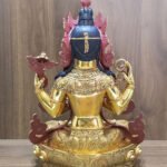 Rear view of Chenrezig statue showing dark blue hair, decorated shoulders and engraved garments and lotus pedestal.