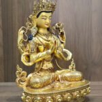 Right-facing view of four-armed Chenrezig statue showing joined hands, prayer beads, lotus and engraved garments.