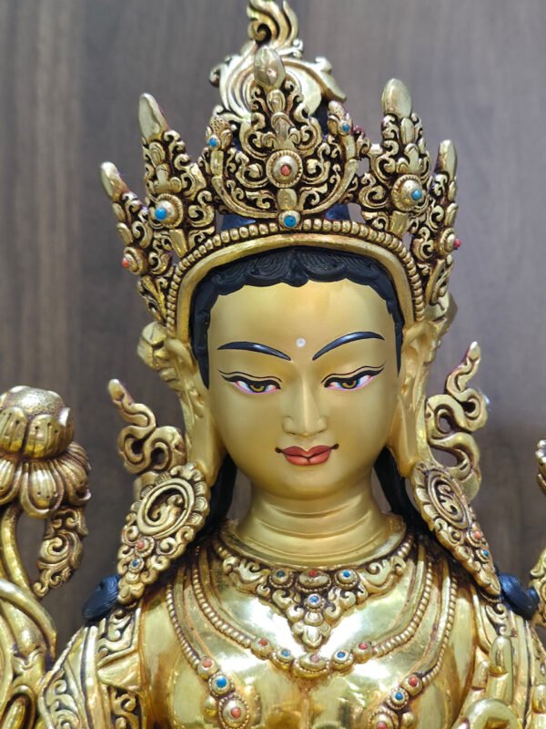 Close-up of the Green Tara statue’s painted face, ornate crown and red and blue decorative accents.