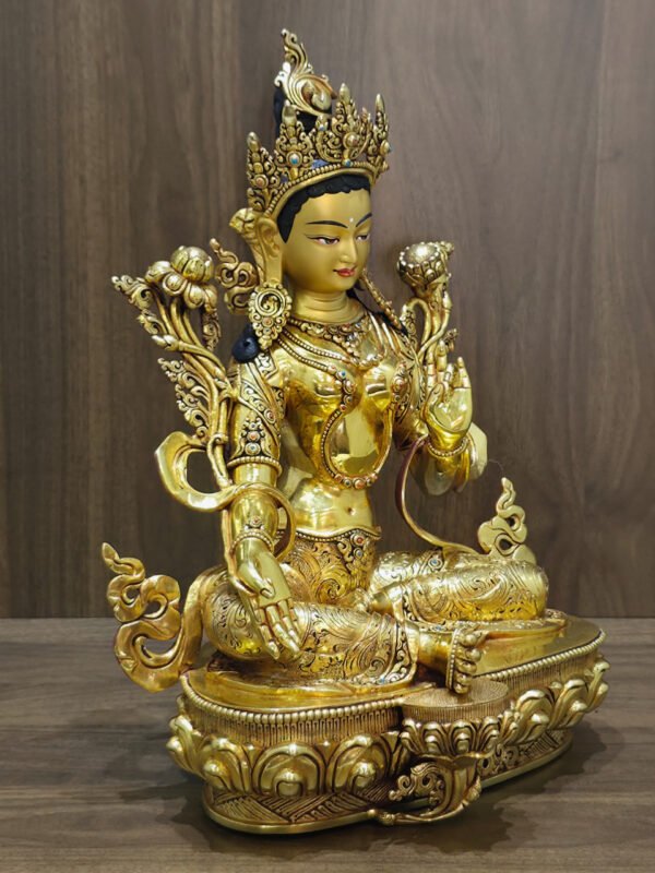 Green Tara statue facing right, showing the shoulder flowers, flowing scarf ornaments and engraved garments against a wood background.