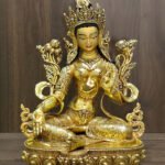 Alternate front view of the Green Tara statue showing the extended right foot, open right palm and shoulder flowers against a wood background.