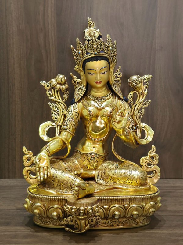 Alternate front view of the Green Tara statue showing the extended right foot, open right palm and shoulder flowers against a wood background.